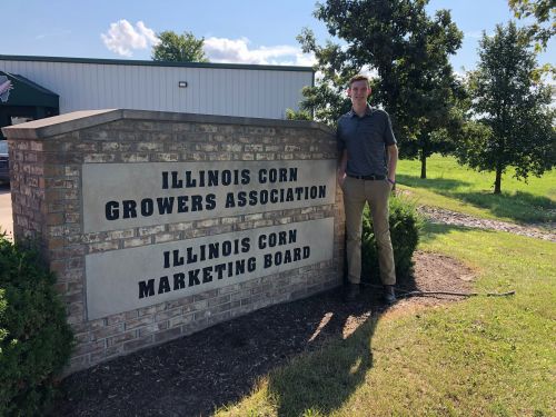 Intern Peter standing in front of IL Corn sign